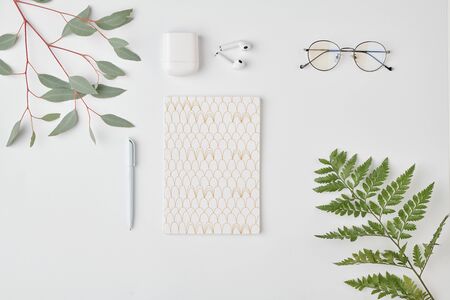 Flatlay of notebook with pen, eyeglasses and earphones on white background surrounded by green...