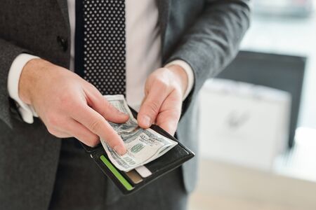 Hands of rich young elegant businessman in suit holding wallet and dollar banknotes while going to pay for somethingの写真素材