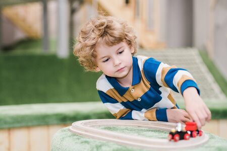 Adorable little boy lying on the floor of playground while playing toy trains