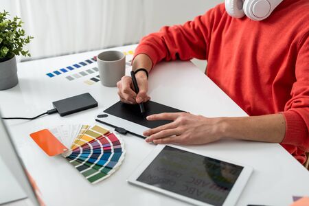 Hands of contemporary freelance designer with stylus over graphics tablet retouching photos by deskの写真素材