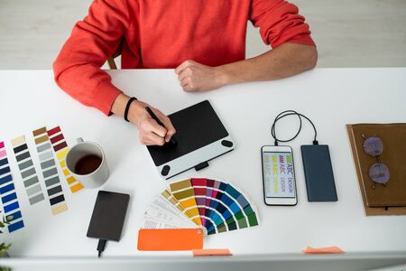 Hands of young male web designer with stylus over graphics tablet screen during retouching work by deskの写真素材