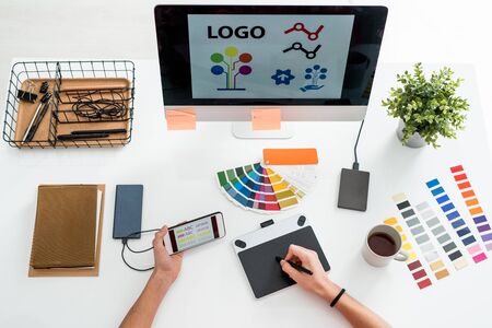 Flat layout of hands of web designer with stylus over screen of graphics tablet choosing printing type for logoの写真素材