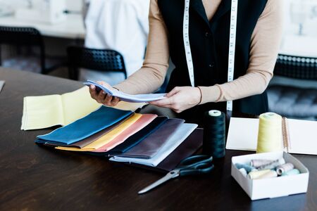 Close-up of unrecognizable tailor with tape measure around neck choosing textile for dress in studioの写真素材