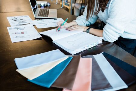 Close-up of unrecognizable woman drawing fashion sketches in notepad while working in tailoring studioの写真素材