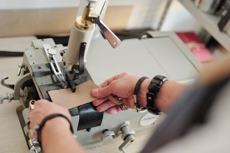Above view of unrecognizable man in bracelets attaching leather piece into machine