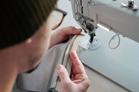 Over shoulder view of hipster craftsman stitching zipper on leather sewing machine