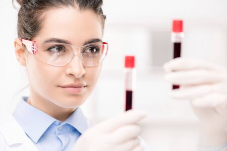 Serious female clinician in protective eyeglasses looking at samples