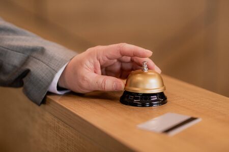 Hand of traveling businessman pushing ring button on wooden reception counterの写真素材