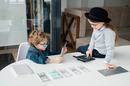 Two adorable economists of elementary age making calculations and financial analysis during working meeting in officeの写真素材