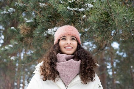 Cute cheerful girl in warm winterwear enjoying winter day in the forest or park