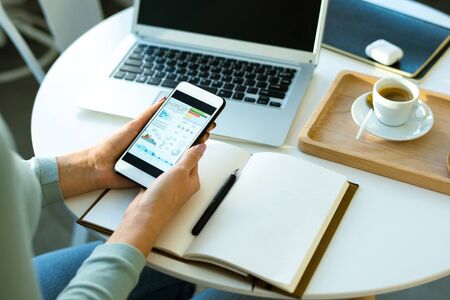 Hands of young economist with smartphone analyzing or looking through financial data while working...
