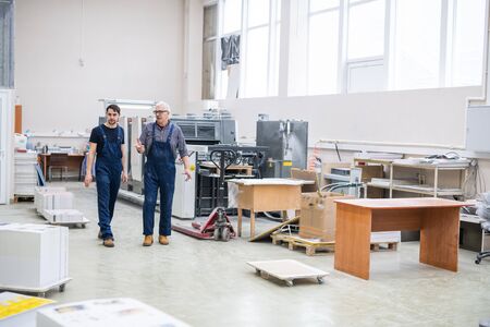 Senior worker giving tour of printing factory to new employee and explaining his duties