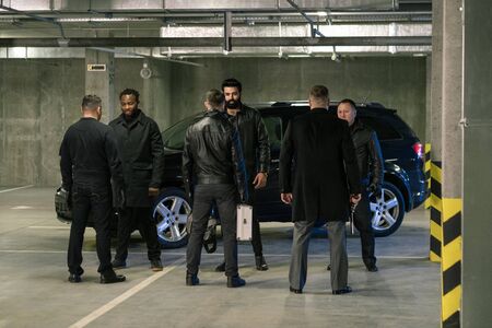 Several intercultural men in black discussing terms of criminal business