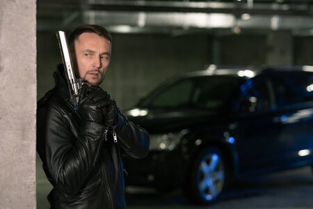 Young killer or agent in black leather jacket and gloves holding handgun