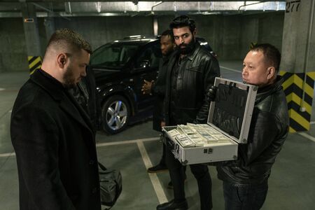 Mature man in black jacket, gloves and jeans opening suitcase with dollars