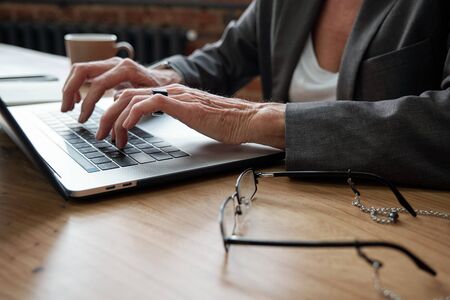 Close-up of unrecognizable businesswoman sitting at table with glasses and preparing presentation on laptopの写真素材