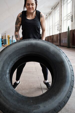 Determined athletic woman with tattooed arms flipping large heavy tire
