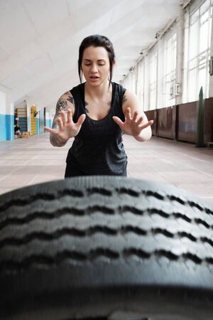 Young Caucasian tattooed female athlete with dark hair throwing heavy tireの写真素材