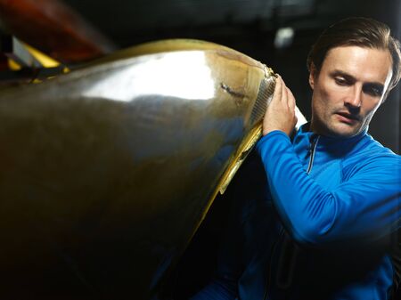 Young concentrated Caucasian sportsman in blue swimming jacket carrying boat before taking part in kayak competitionの写真素材
