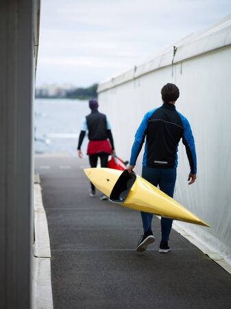 Rear view of two unrecognizable male athletes in swimming sportswear going towards river and...