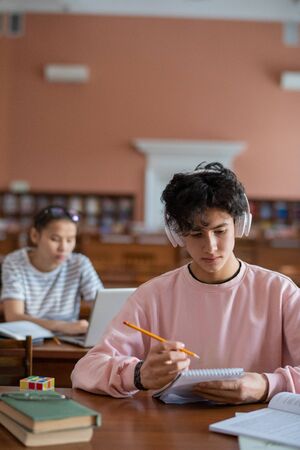 Serious college student in headphones listening to music while reading his notesの写真素材