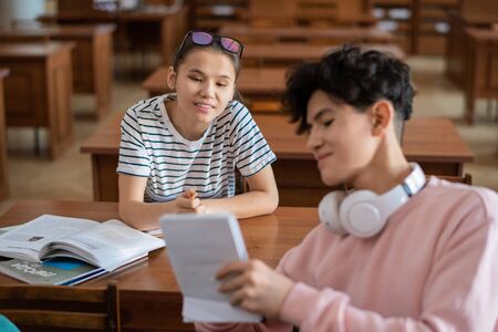 Clever teenage girl pointing at notes in notepad of classmate during discussion