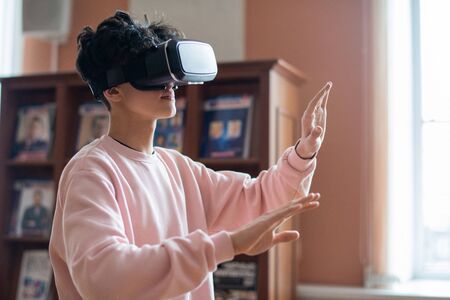 Mobile college student in casualwear and vr goggles touching virtual screen while moving in three dimensional realityの写真素材