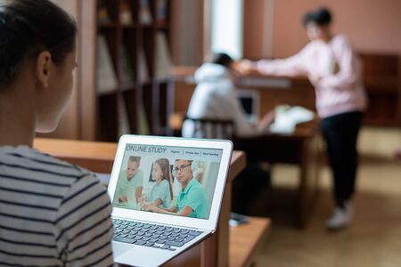 Laptop display with homepage of educational website and contemporary teenage student sitting in front and studyingの写真素材