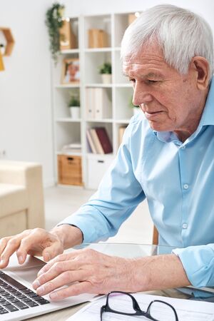 Aged retired man pressing keys of laptop keypad while surfing in the net