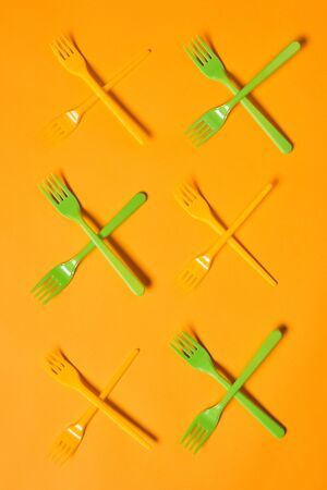 Vertical conceptual flat lay shot of X marks made of disposable light green and orange plastic forks...