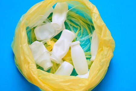 Horizontal from above flat lay shot of yellow plastic garbage bag with plastic litter in it on blue...