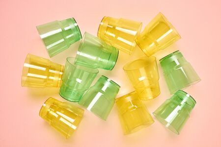 Horizontal from above flat lay shot of transparent green and yellow plastic cups lying on neutral...