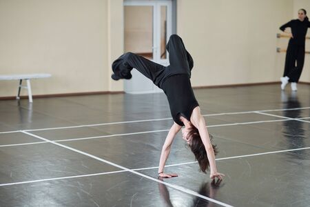 Young female dancer wearing black outfit doing difficult handspring element, horizontal shot