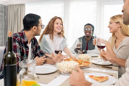 Multi-ethnic group of five friends relaxing at dinner table together at weekend, horizontal shot
