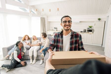Young Middle-Eastern man gets pizza delivered for friends gathering in modern apartment, horizontal...