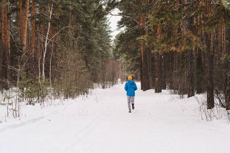 Rear view of unrecognizable man in blue jacket running in winter forestの写真素材