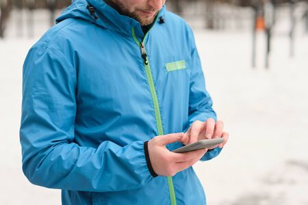 Close-up of man in blue jacket standing outdoors and using smartphone while watching video with...