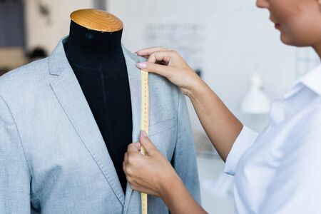 Young fashion designer with yellow tape measuring length of jacket collarの写真素材