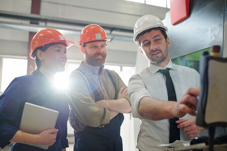 Confident businessman in hardhat and formalwear pointing at control panel