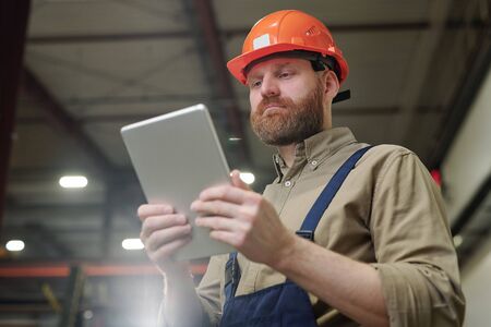Young engineer with red beard holding tablet while scrolling through online data
