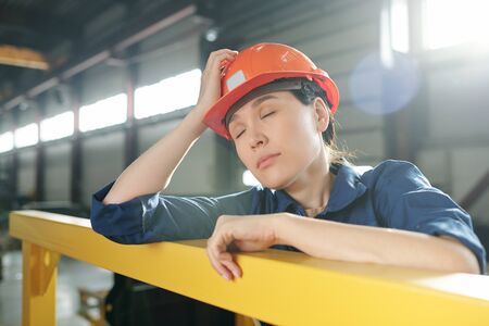 Tired young female engineer in workwear and hardhat napping by barの写真素材