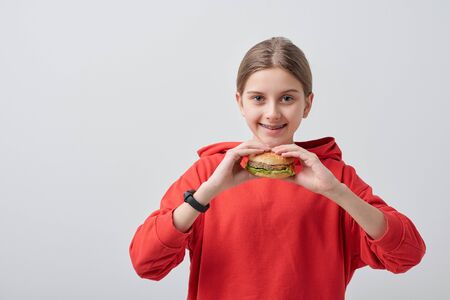 Portrait of smiling teenager in red sweatshirt eating burger against white backgroundの写真素材