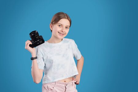 Portrait of smiling pretty teenage girl posing with professional camera against blue backgroundの写真素材