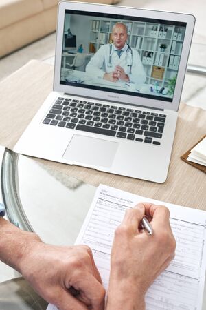 Medical specialist consulting senior man on health insurance claim online, unrecognizable senior man...