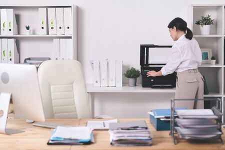Rear view of office manager in blouse choosing amount of copies while making scan of documents on...