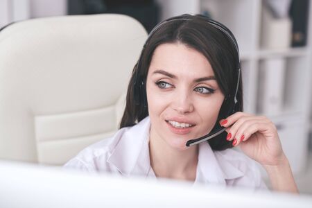 Positive attractive young female call center operator in hands-free microphone answering questions...