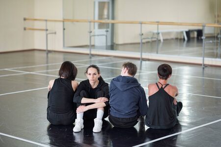 Young serious woman looking at camera while sitting among three dancersの写真素材