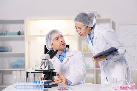Two young intercultural scientists in whitecoats working over new vaccine