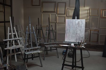 Interior of contemporary arts school or studio with unfinished picture on one of easels and painting stuff near byの写真素材