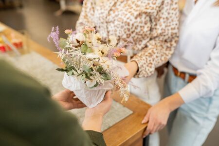 Hands of young owner of florist shop holding bunch of flowers over counterの写真素材